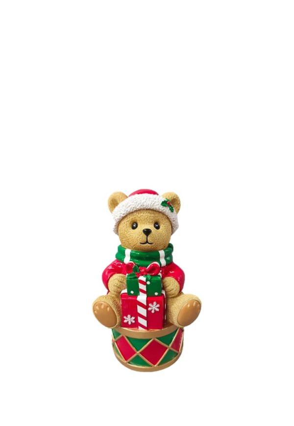 A small teddy bear Christmas ornament wearing a red and white Santa hat, a green and red striped sweater, and holding a red and green gift box, sitting on a matching drum base against a white background.