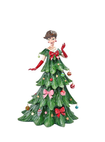 A decorative figurine of a woman with short brown hair wearing a green Christmas tree dress with red gloves and red and pink bows, decorated with ornaments, on a plain white background.