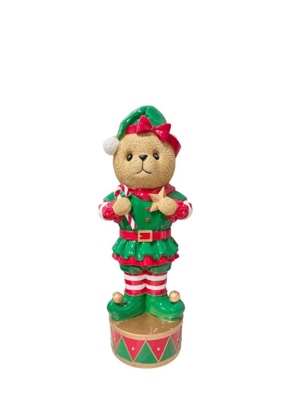 A Christmas-themed teddy bear figurine dressed as an elf, standing on a decorated base against a plain white background.