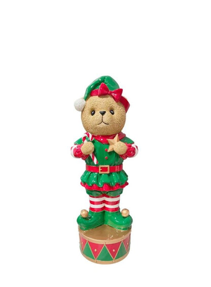 A Christmas-themed teddy bear figurine dressed as an elf, standing on a decorated base against a plain white background.