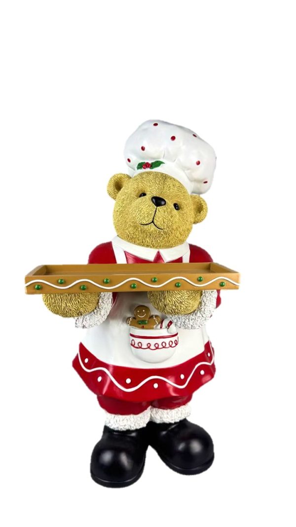 A festive teddy bear figurine dressed as a chef, holding a wooden serving tray. The bear has a golden-brown fur coat, wearing a white chef's hat with red polka dots, a red and white apron with green accents, and black boots.