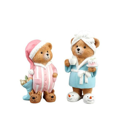 A pair of teddy bear figurines dressed as a couple. One bear wears a pink and white striped pajama set with a pink hat and holds a blue mug.