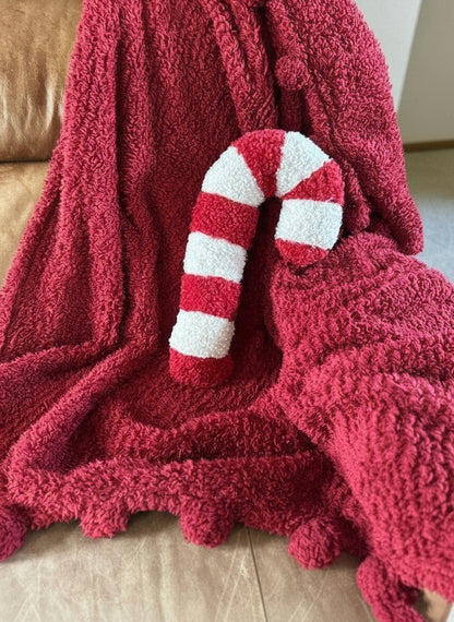 Red Candy Cane Sherpa Pillow sitting on a red fluffy blanket 