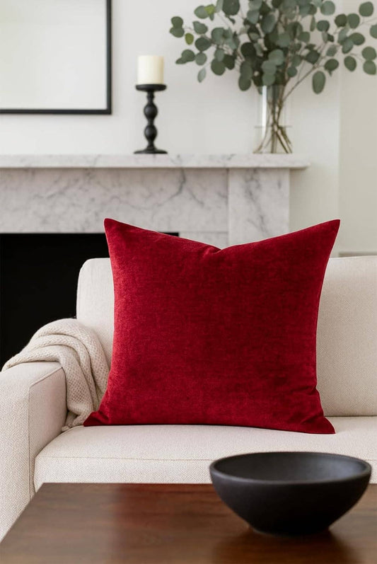 Red pillow on a beige sofa with a marble fireplace and decorative elements in the background.