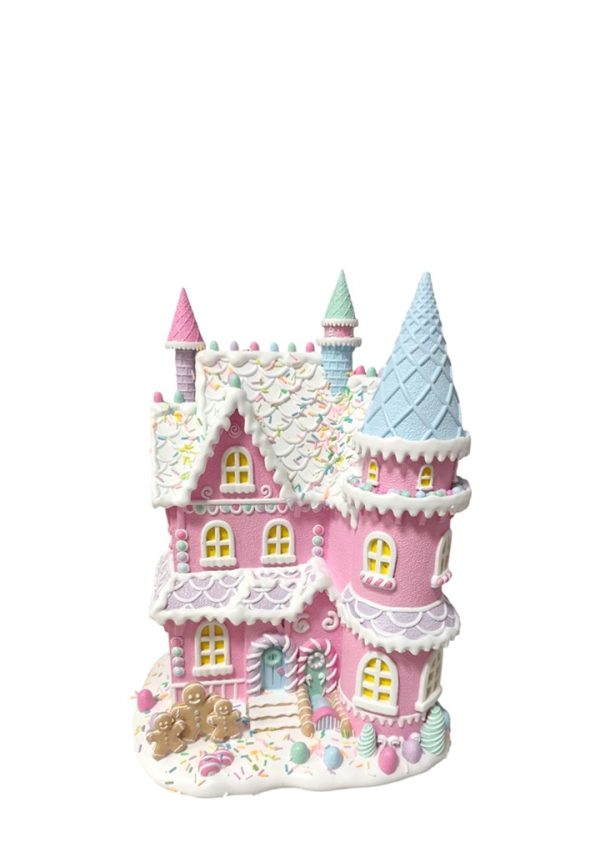 A whimsical pink fairy tale castle decoration with white icing-like trim, a light blue conical tower, pastel multicolor sprinkles, and small gingerbread figures at the base, shown on a plain white background.